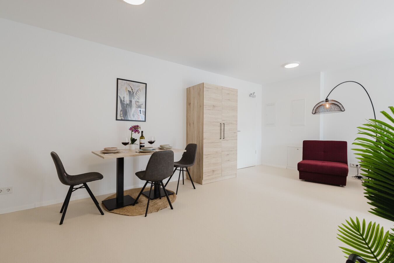 A modern, minimalist room with a dining area, a red sofa, and a large plant.