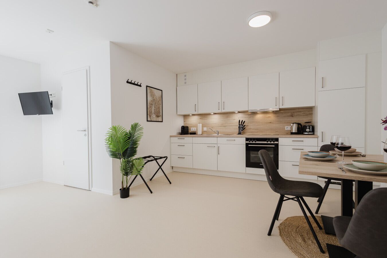 A modern kitchen with white cabinets, a black countertop, and a dining area with a table and chairs.