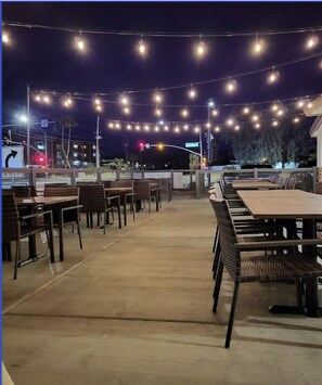 Outdoor dining area with tables and chairs, illuminated by string lights.