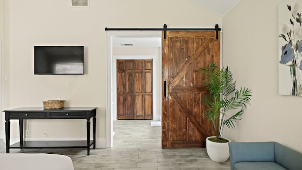 A room with a sliding barn door, a television mounted on the wall, a console table, a potted plant, and a blue sofa. - Charming Round Rock Retreat (Round Rock)