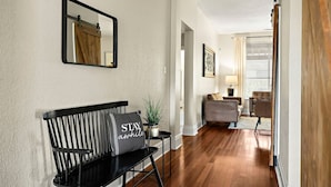 A hallway with a black bench, a mirror, and a cushion with "STAY awhile" text. There are two sofas in the background. - Charming Round Rock Retreat (Round Rock)