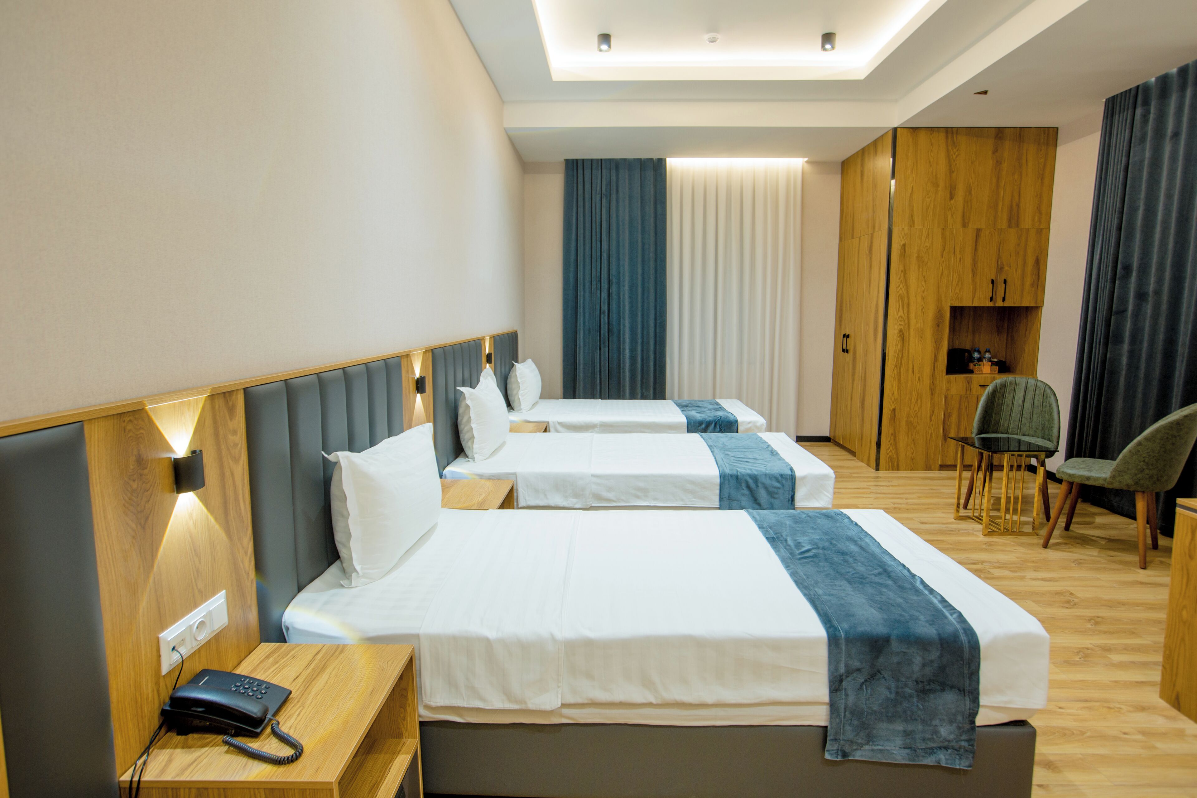 A hotel room with two beds, a wooden wardrobe, a desk with a telephone, and a chair.
