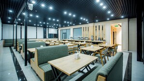 Un comedor moderno con cabinas y mesas, una cocina al fondo y un techo con diseño de cuadrícula.