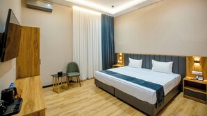 Habitación de hotel con cama, escritorio, silla, televisor y mesita de noche con lámpara.
