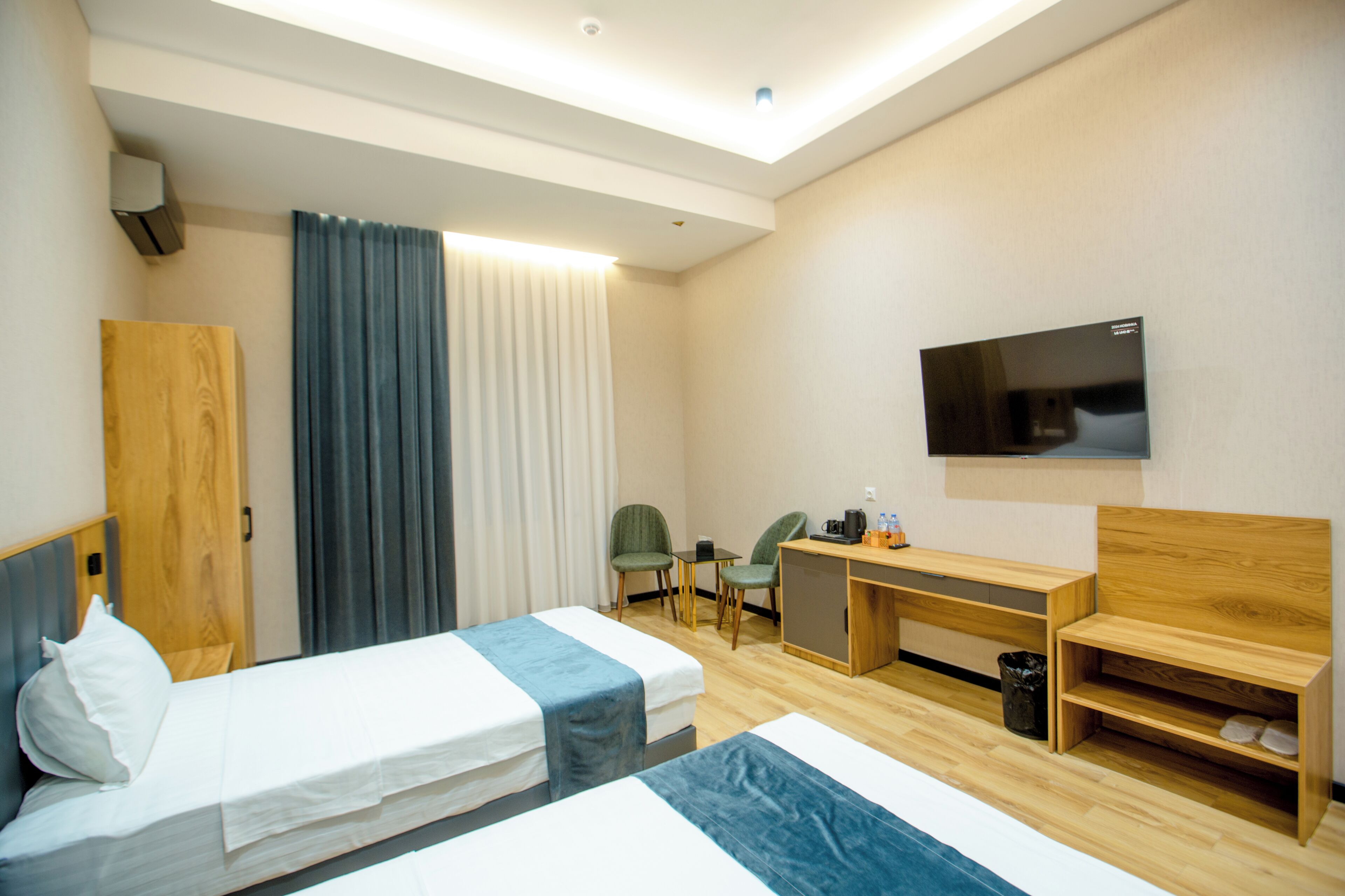 A hotel room with two beds, a desk, a chair, a TV, and a small trash bin.
