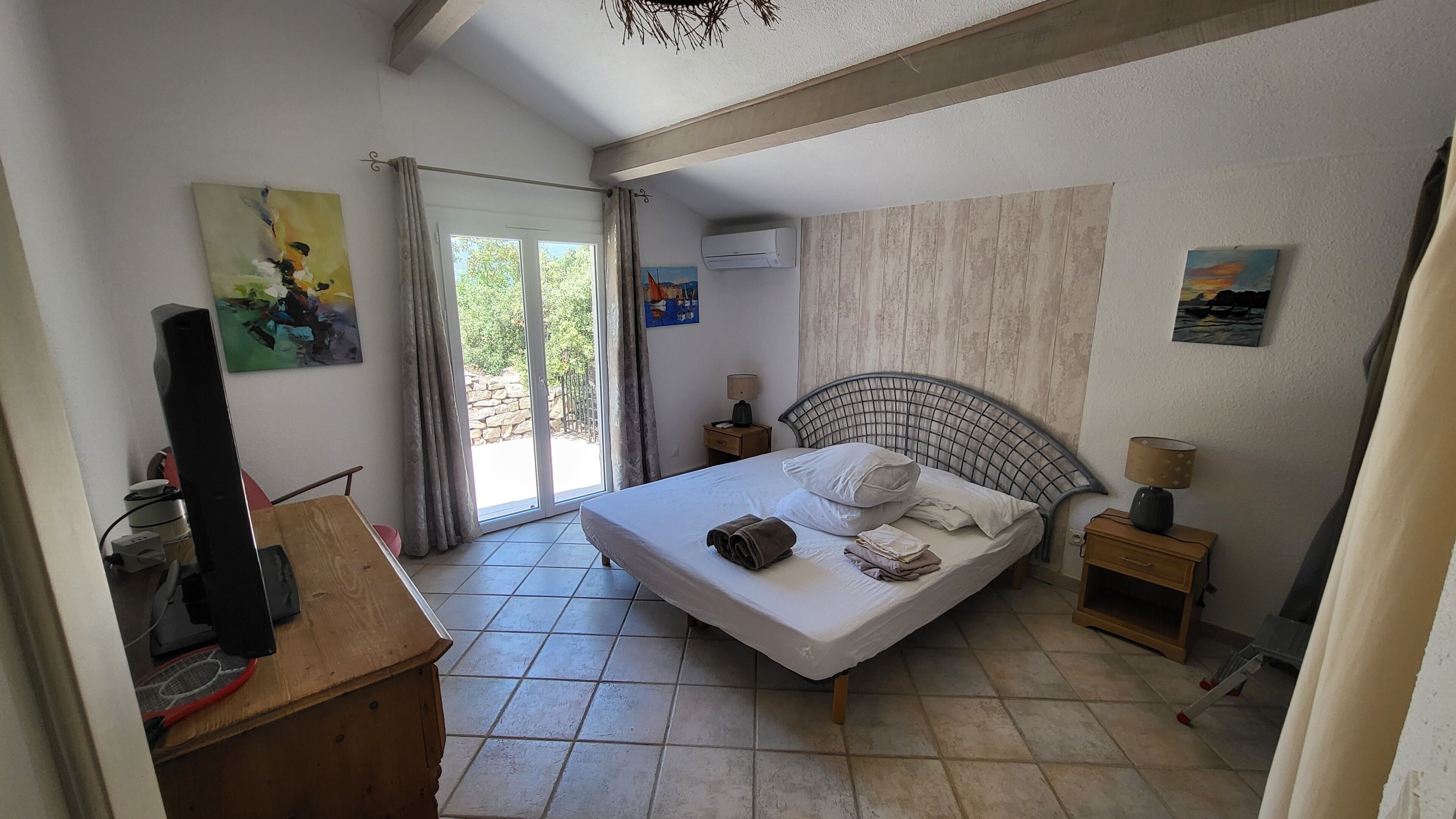 A bedroom with a bed, a desk, a television, and artwork on the walls.