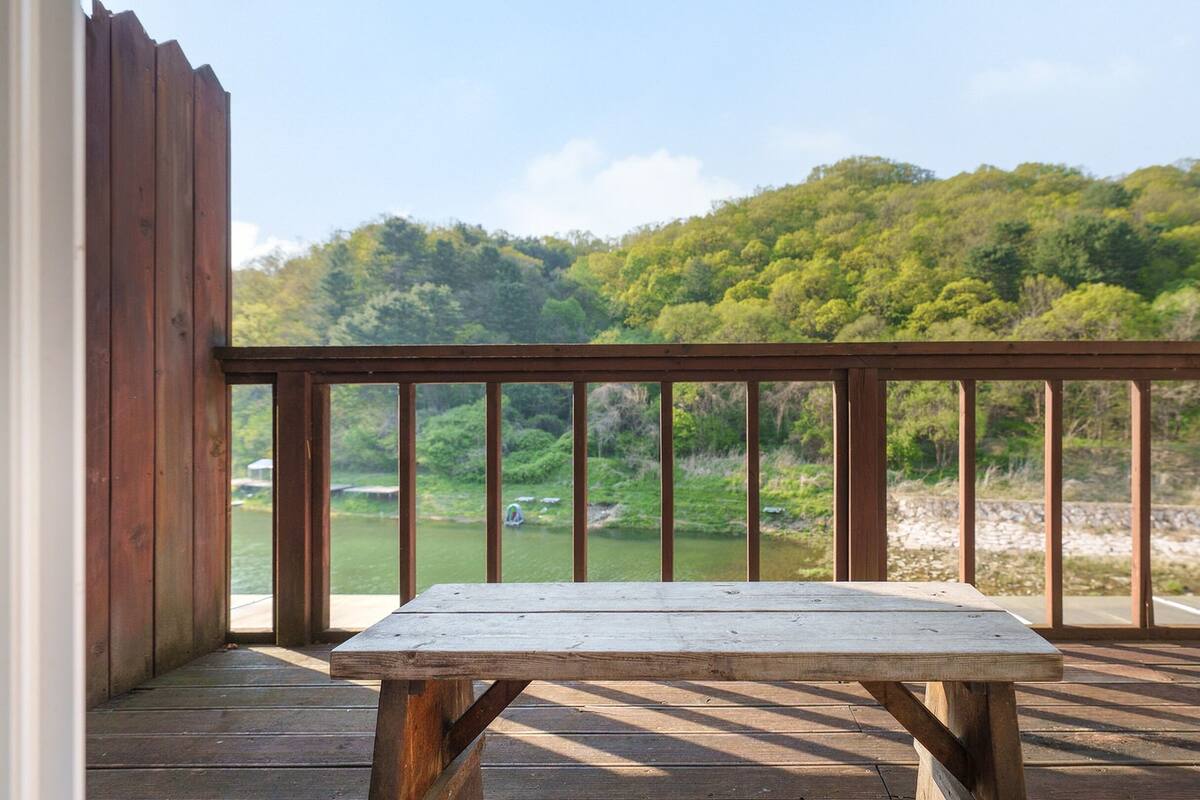 Una terraza de madera con una mesa de picnic, con vista a un río y colinas boscosas.