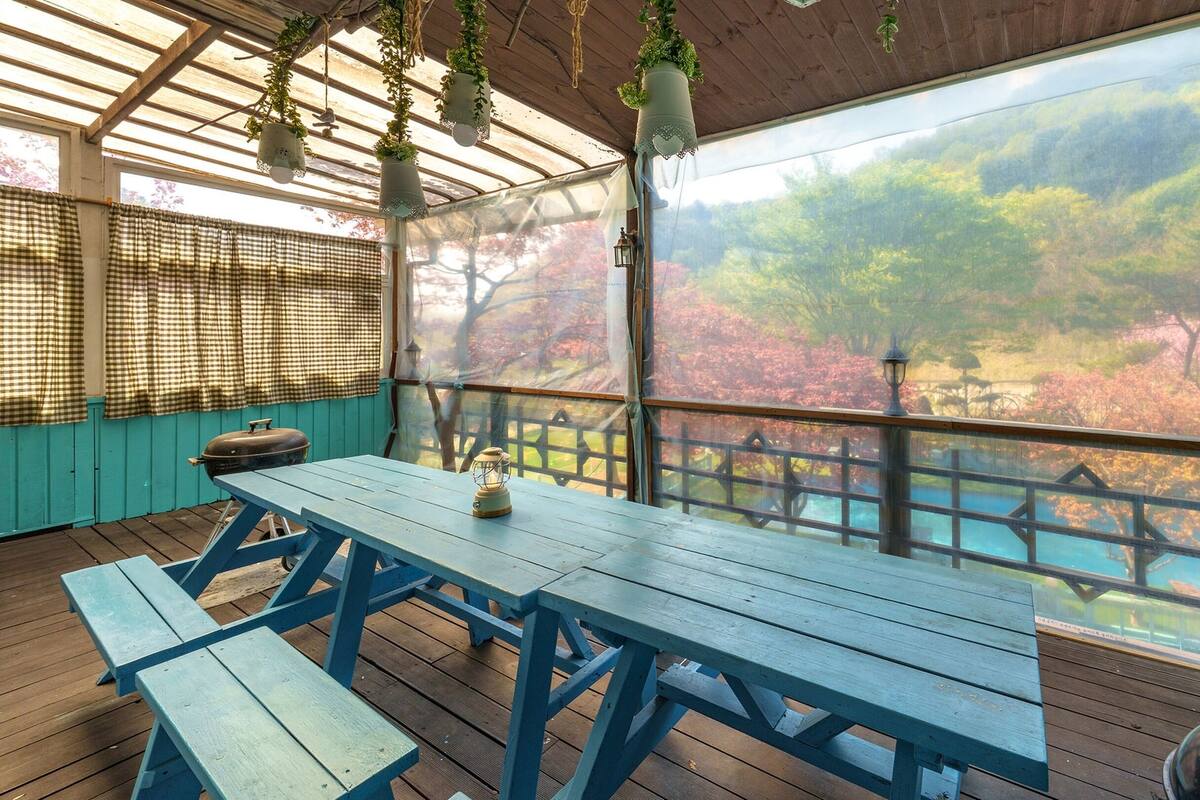 Un área de estar al aire libre cubierta con una mesa y bancos, con vistas a un paisaje pintoresco con árboles y una masa de agua.