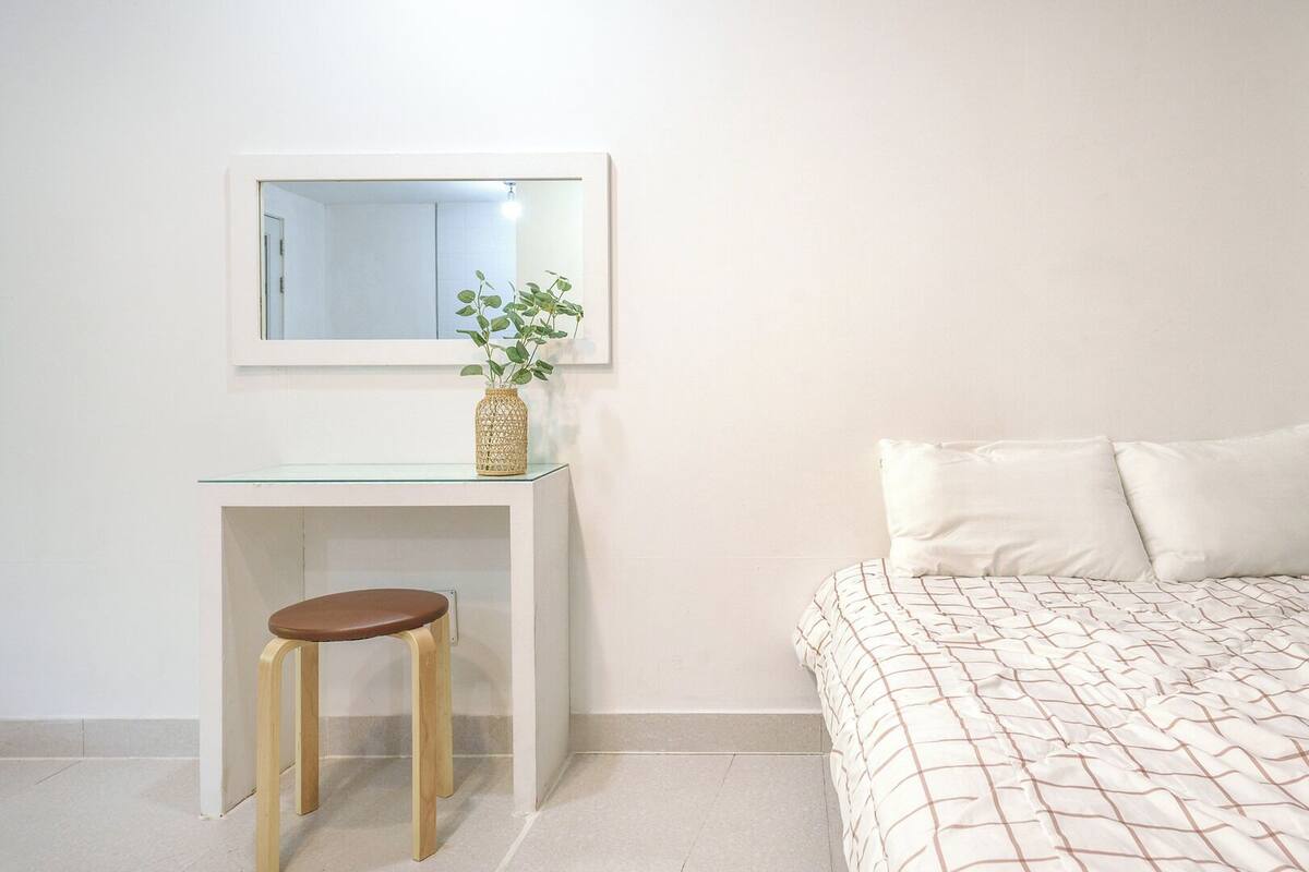 Un dormitorio con una cama, un escritorio pequeño con un taburete, un espejo y una planta.