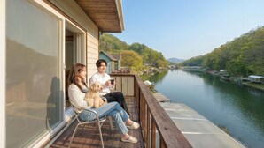 Ein Paar sitzt auf einer Holzterrasse mit Blick auf einen Fluss, ein Hund ist in ihrer Nähe.