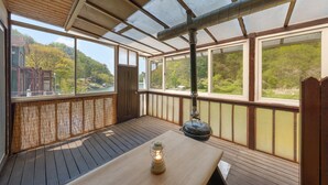 Eine überdachte Terrasse im Freien mit einem Holztisch und einer Laterne, große Fenster mit reizvollem Blick.