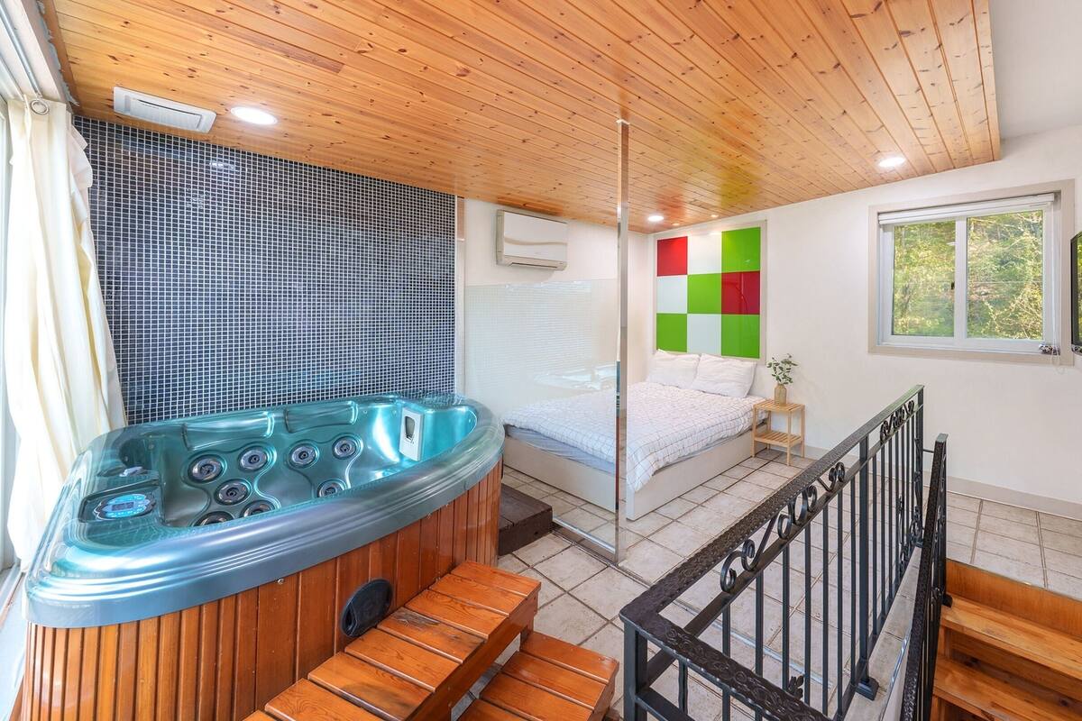 Una habitación con techo de madera, bañera de hidromasaje, cama y ventana con vistas a árboles.
