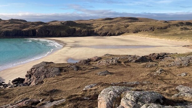 Un paysage côtier avec une plage de sable, des affleurements rocheux et un ciel dégagé.