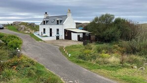Une maison blanche à deux étages, avec un toit en pente, une cheminée et un petit garage attenant.