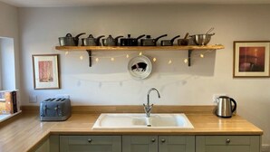 Une cuisine avec un plan de travail en bois, un évier, un grille-pain, une bouilloire et une étagère où sont rangées des casseroles et des poêles.