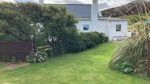 Une maison blanche avec un toit gris, entourée d’une pelouse bien entretenue et d’une végétation dense.