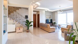 A spacious living area with a curved ceiling, a staircase with ornate railings, a flat-screen TV, and a large window with a view. - Villa La mer de Crete - private pool & sew view (Agia Pelagia)