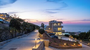 A coastal residential area with modern houses, a paved walkway, and a view of the sea at dusk. - Villa La mer de Crete - private pool & sew view (Agia Pelagia)