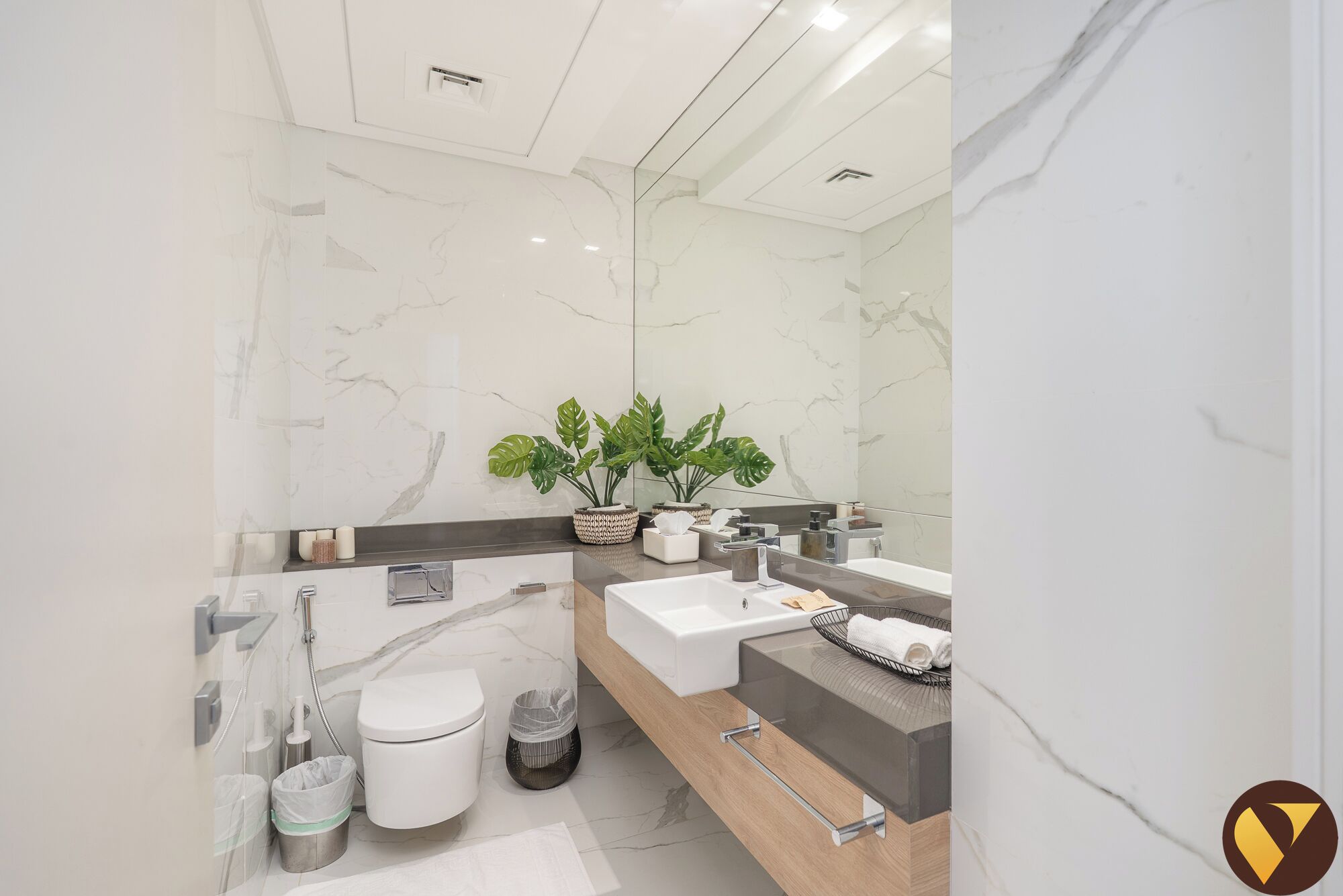 A modern bathroom with a marble floor, a white toilet, a shower, and a vanity with a sink and mirror.