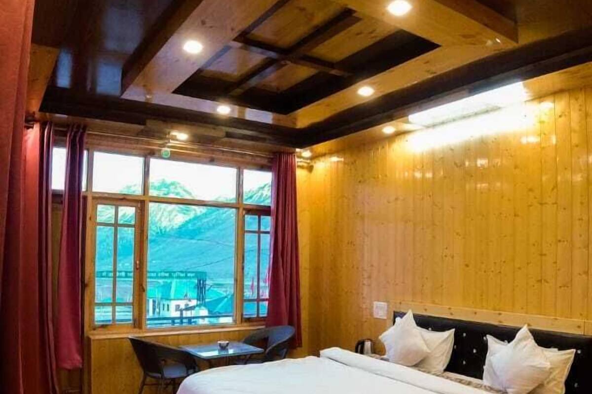 A wooden room with a bed, a desk, and a window with a mountain view.