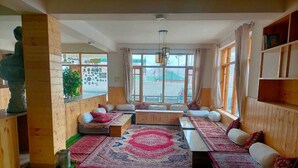 A cozy room with a large window, wooden furniture, and a patterned rug. - Kapoor Resort Kaza by Mountain Bee (Kaza)