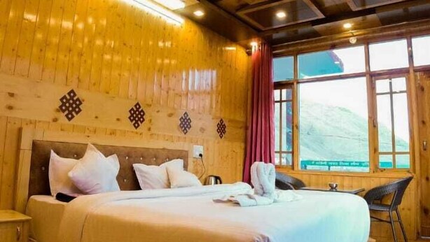 A wooden room with a large bed, wooden walls, and a window with a view. - Kapoor Resort Kaza by Mountain Bee (Kaza)