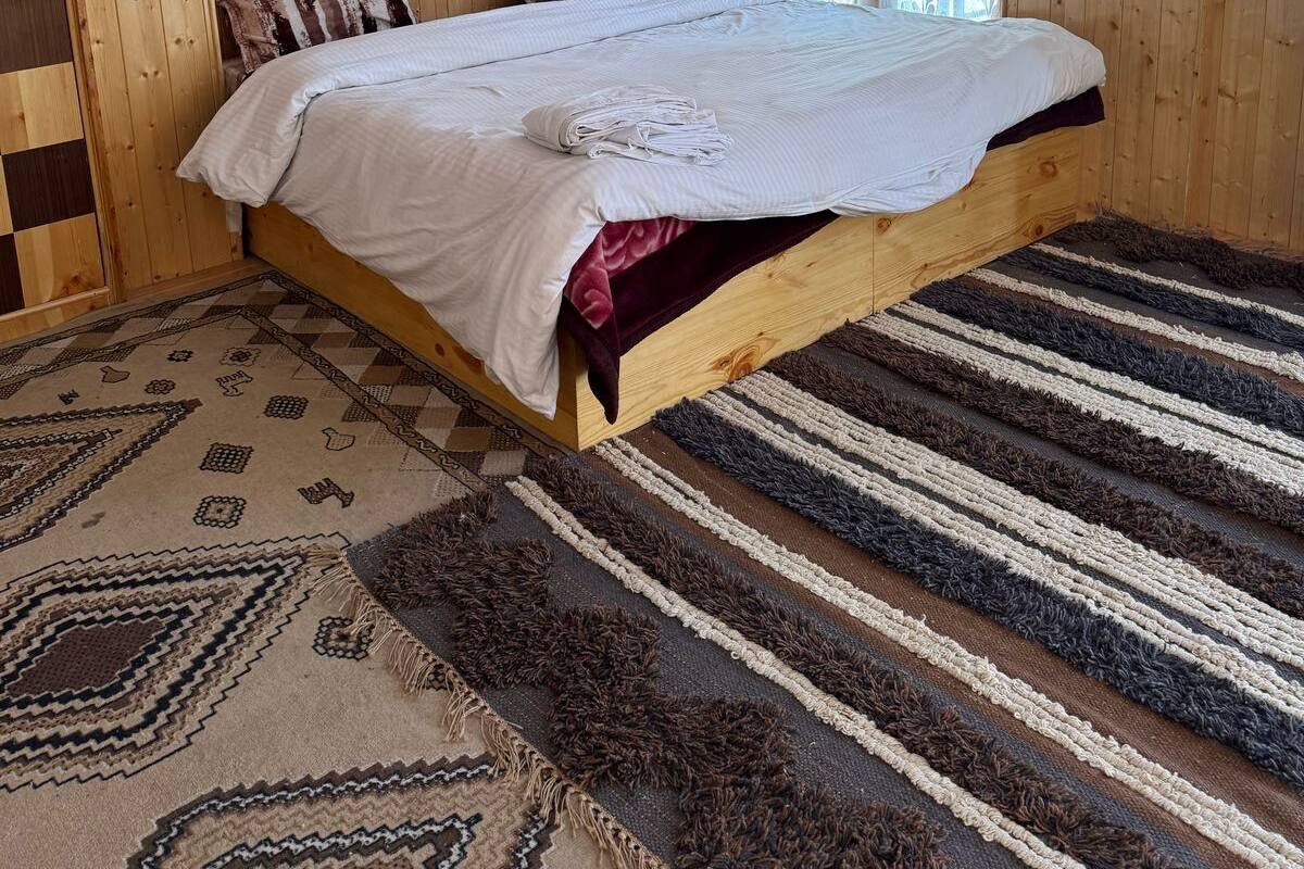 A wooden-paneled bedroom with a bed, a patterned rug, and a window with curtains.