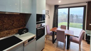 Une cuisine moderne dotée d’appareils électroménagers intégrés, un coin repas avec une table et des chaises en bois, et une grande fenêtre offrant une vue sur l’extérieur.