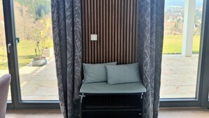 Une pièce offrant une vue sur un paysage montagneux grâce à de grandes fenêtres, un mur en lambris de bois et un banc rembourré agrémenté de coussins.