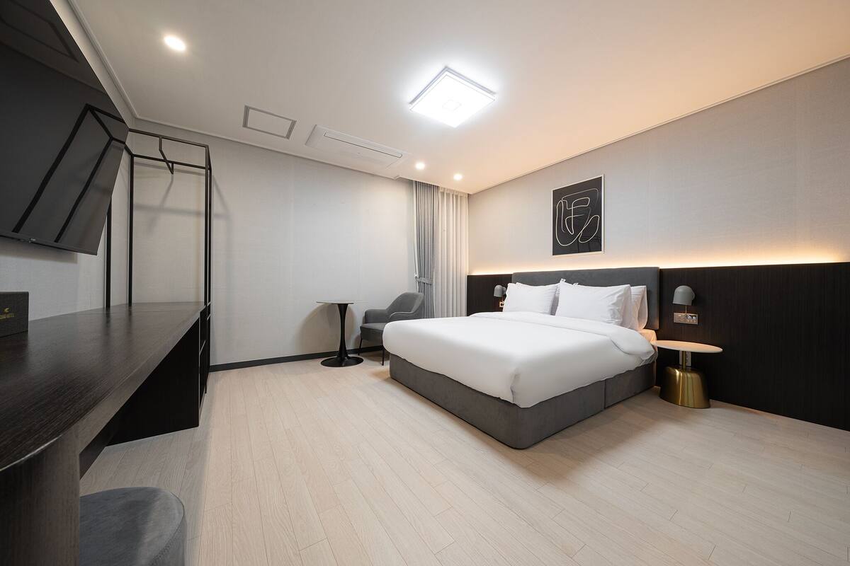 A modern hotel room with a large bed, a desk, a chair, and a flat-screen TV.