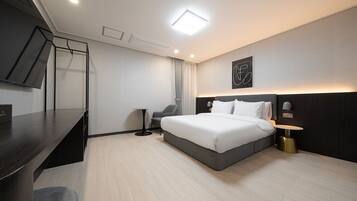 A modern hotel room with a large bed, a desk, a chair, and a flat-screen TV.