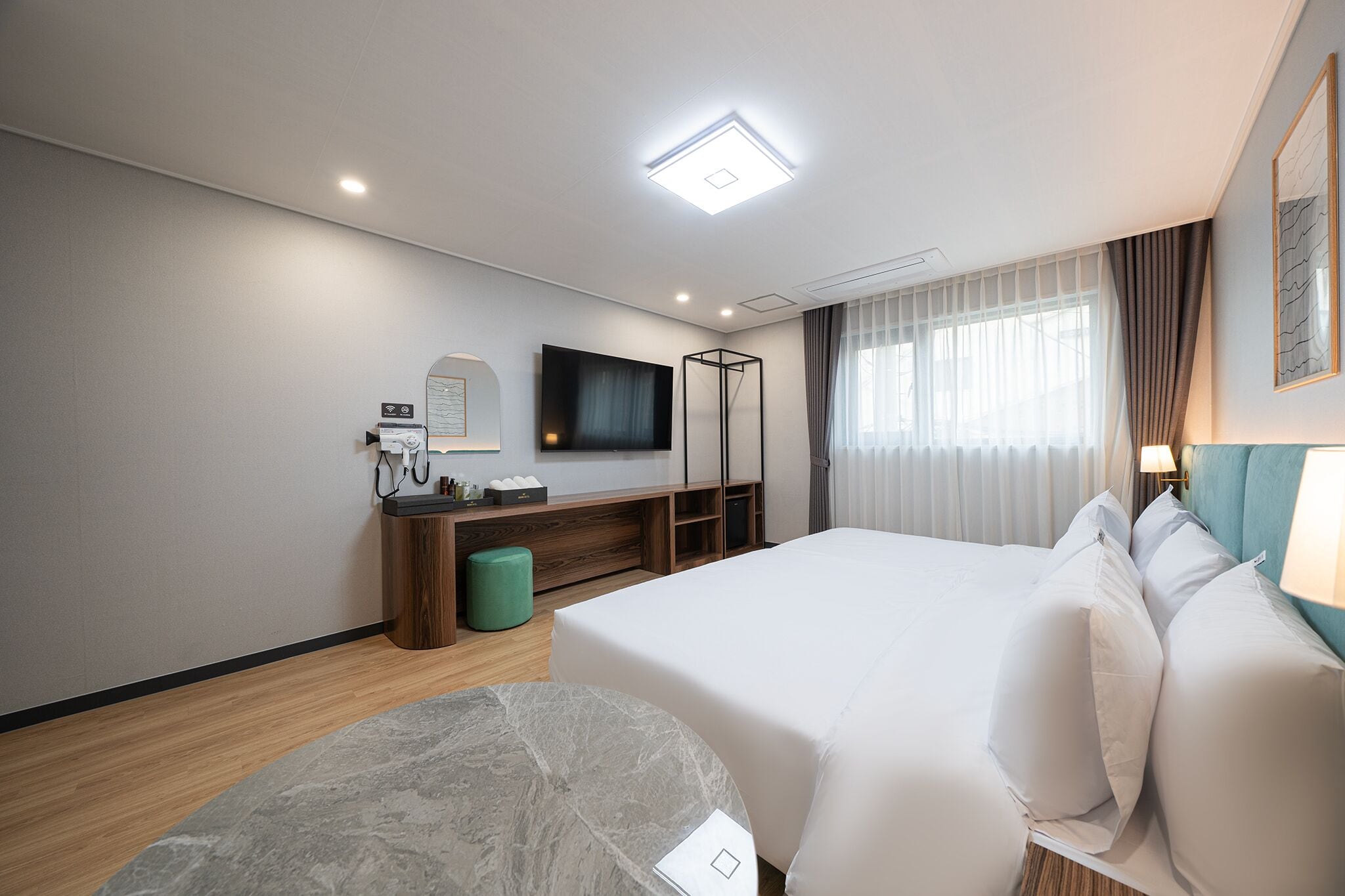 Quarto de hotel com uma cama grande, uma escrivaninha com computador, uma televisão de tela plana e uma janela com cortinas.