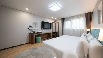Quarto de hotel com uma cama grande, uma escrivaninha com computador, uma televisão de tela plana e uma janela com cortinas.