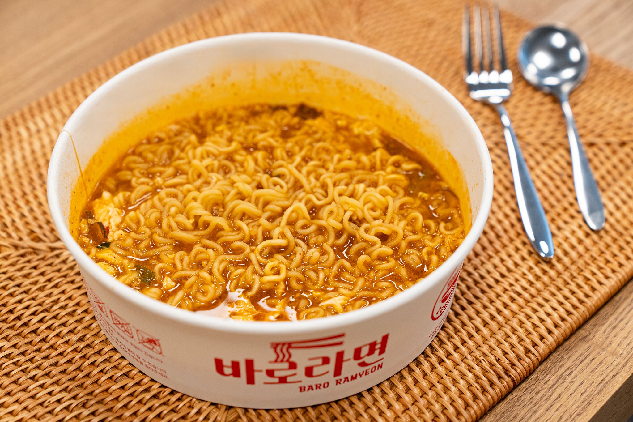 A bowl of instant noodles with a spoon and fork beside it.
