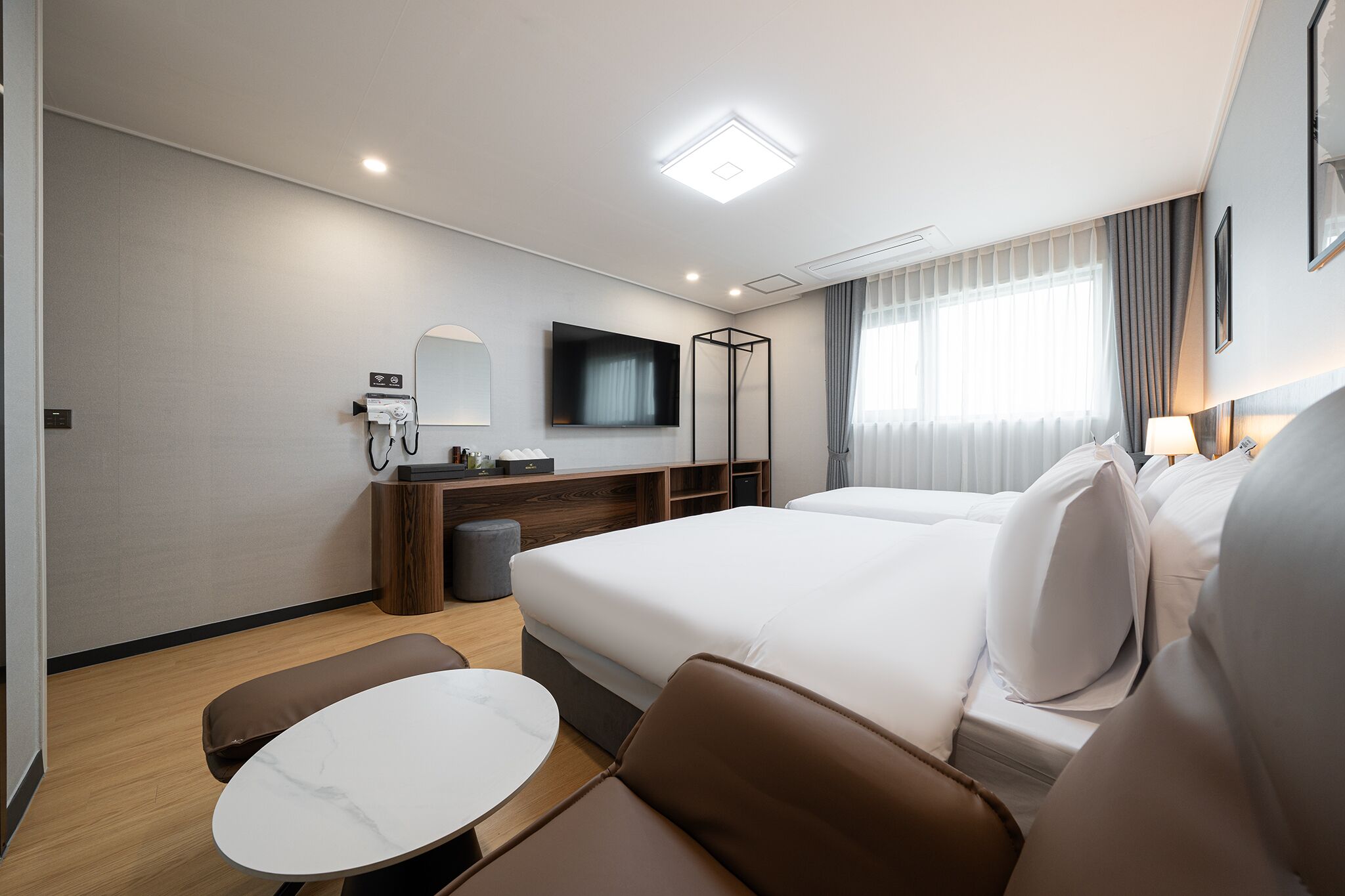 Moderni hotellihuone, jossa on suuri sänky, työpöytä tietokoneella, televisio sekä oleskelualue, jossa on pöytä ja tuolit.