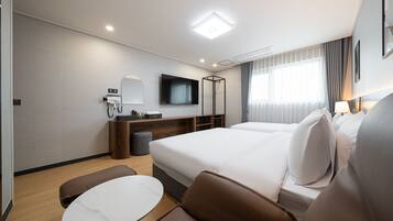 Moderni hotellihuone, jossa on suuri sänky, työpöytä tietokoneella, televisio sekä oleskelualue, jossa on pöytä ja tuolit.