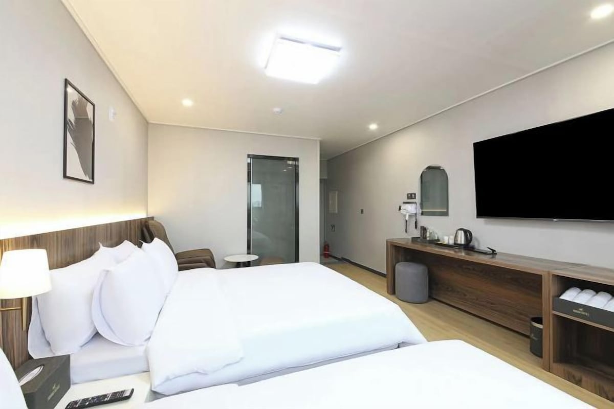 Una habitación de hotel con cama, mesita de noche, lámpara, televisor y una pequeña zona de estar.