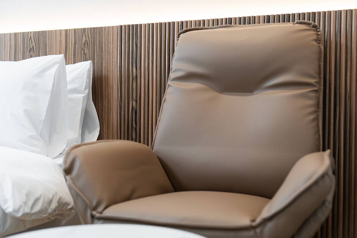 A modern room with a brown leather chair, white pillows, and a wooden panel wall.