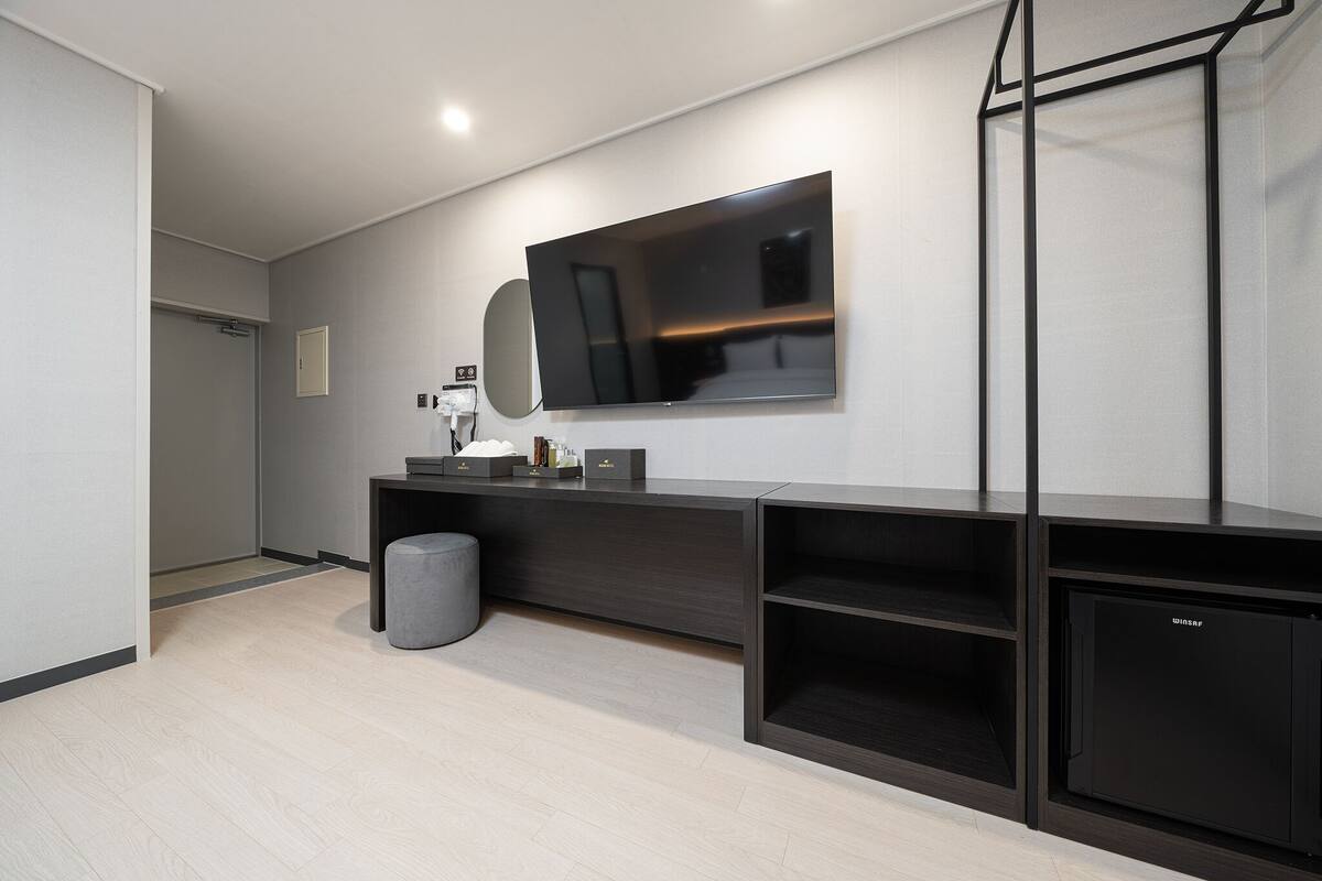 A modern bathroom with a large mirror, a flat-screen TV, and a dark wooden vanity.