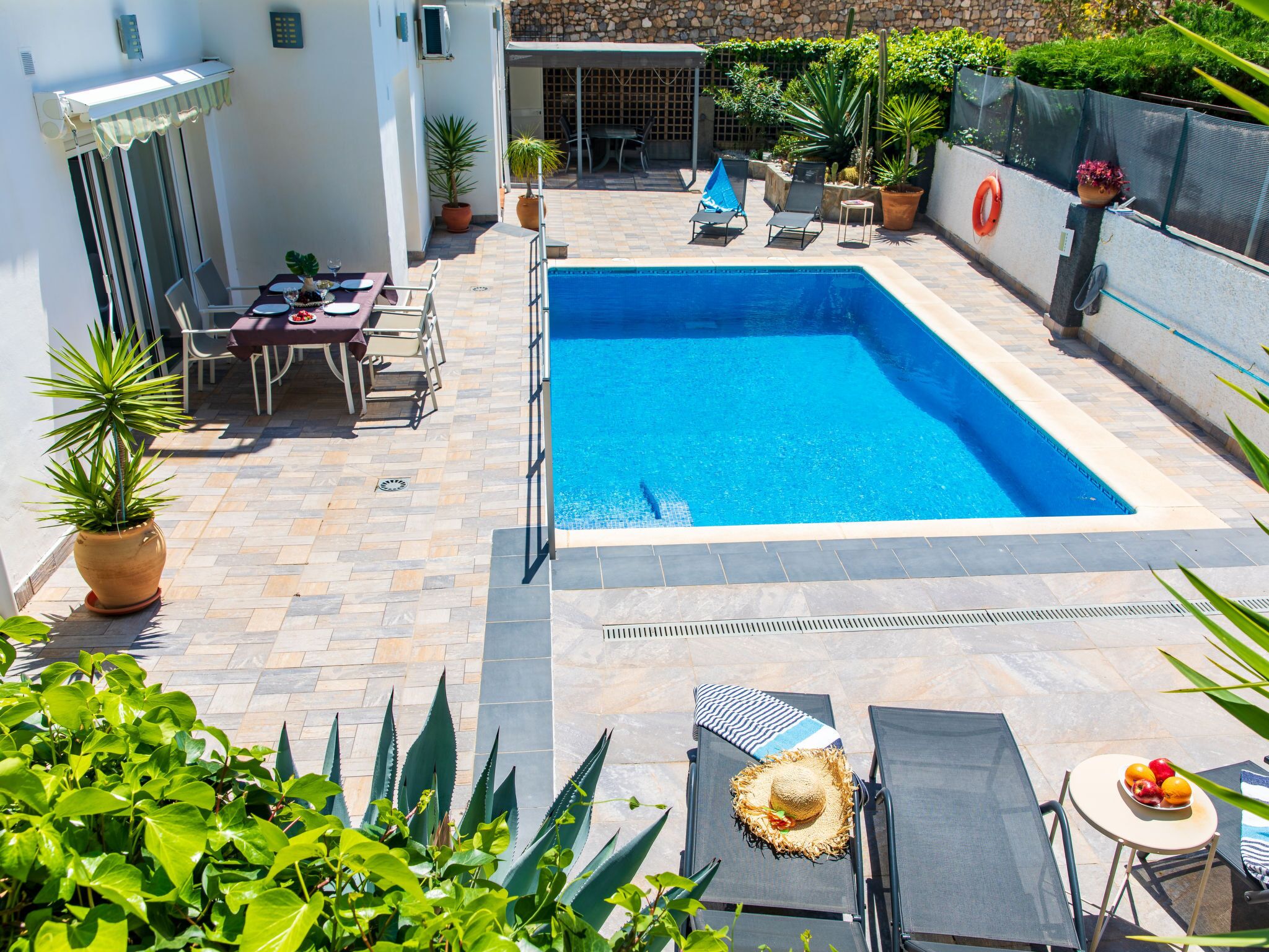 Une piscine entourée d’une terrasse carrelée, de chaises longues et de plantes en pot.
