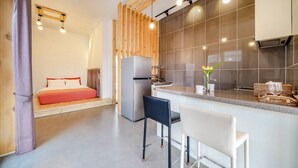 A compact hotel room with a bed, a kitchenette, a bar area, and a seating space.