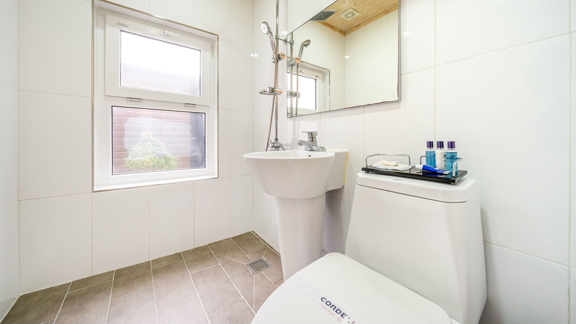 A bathroom with a window, a sink, a mirror, and a toilet.