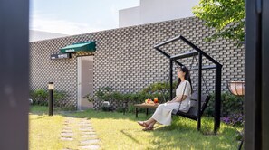 A person sitting on a swing chair in a garden area with a brick wall and a sign that reads 'earldelta'. - Buan Cordelia Pool Villa Pension (Buan)