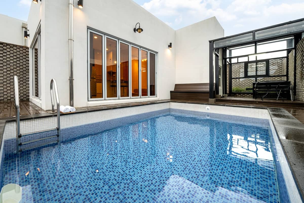 Une piscine dotée d’une terrasse carrelée, d’un espace salon couvert et d’un bâtiment avec de grandes fenêtres.