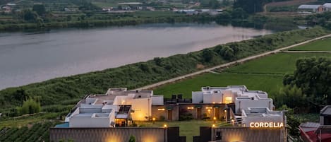 A modern hotel with a rooftop terrace overlooking a river, surrounded by lush greenery.
