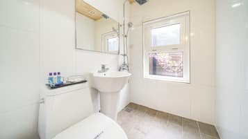 A bathroom with a white sink, a mirror, a window, and a shower.