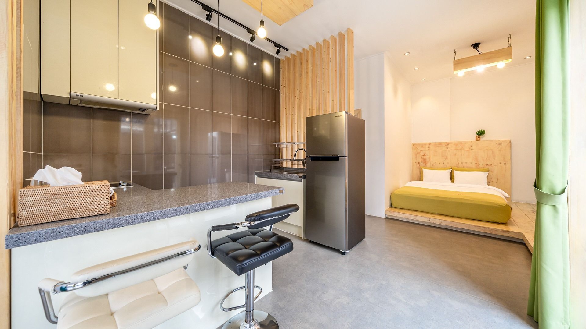A compact kitchenette with a stainless steel refrigerator, a sink, and a bar stool.