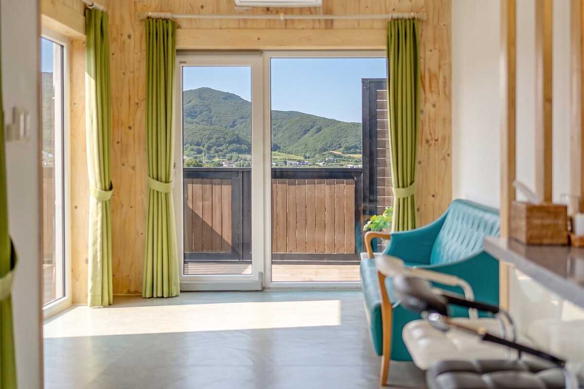 A room with a sliding glass door leading to a balcony with a view of a hilly landscape.