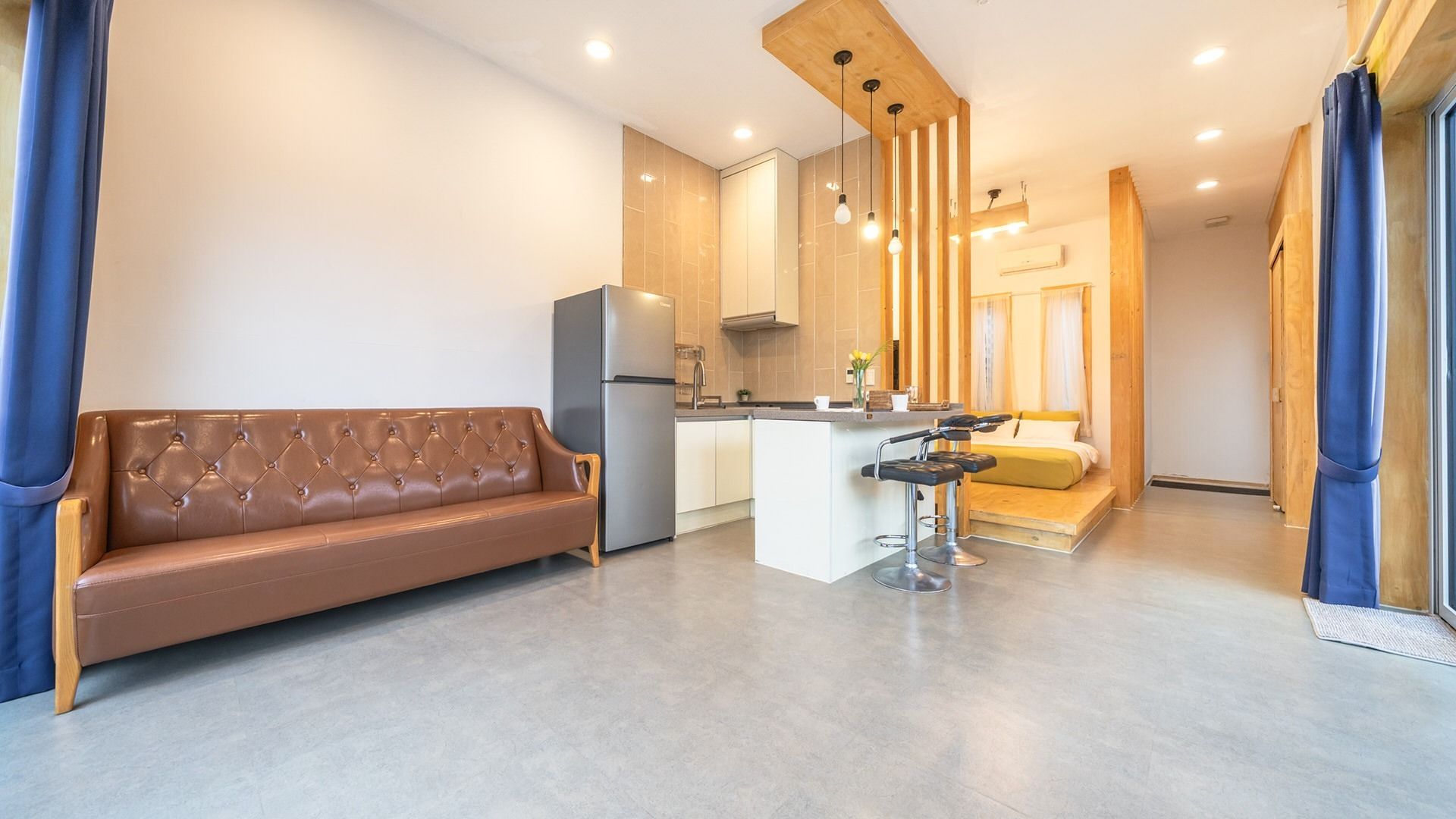 A modern apartment with a kitchenette, a sofa, a dining area, and a bedroom.