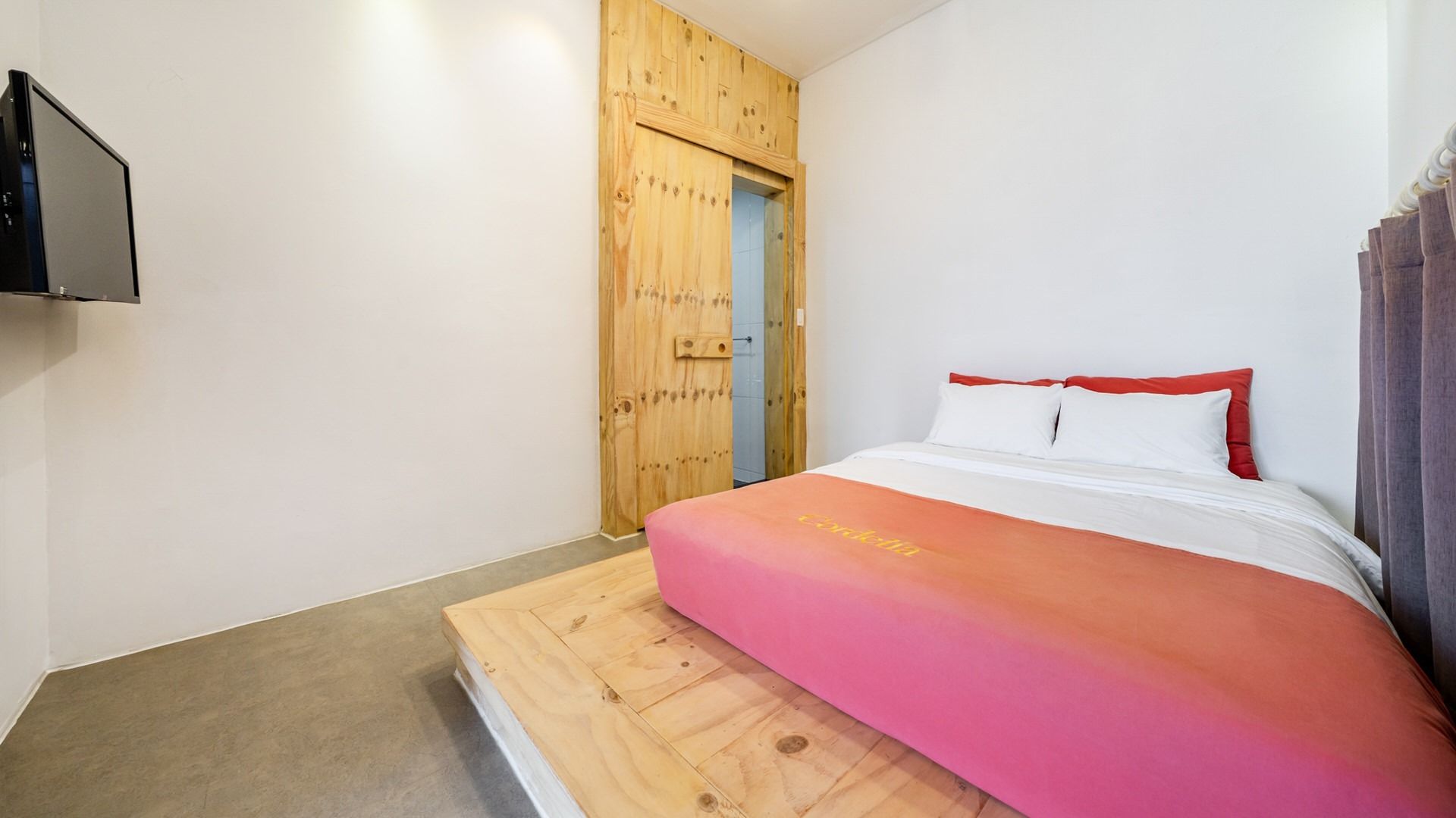 A bedroom with a bed, a wooden wardrobe, and a television mounted on the wall.